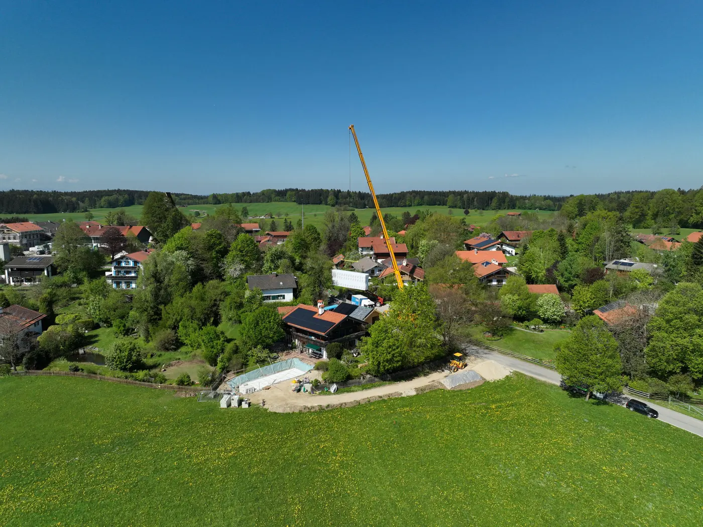 Autokran über dem Grundstück, dahinter das Voralpenland
