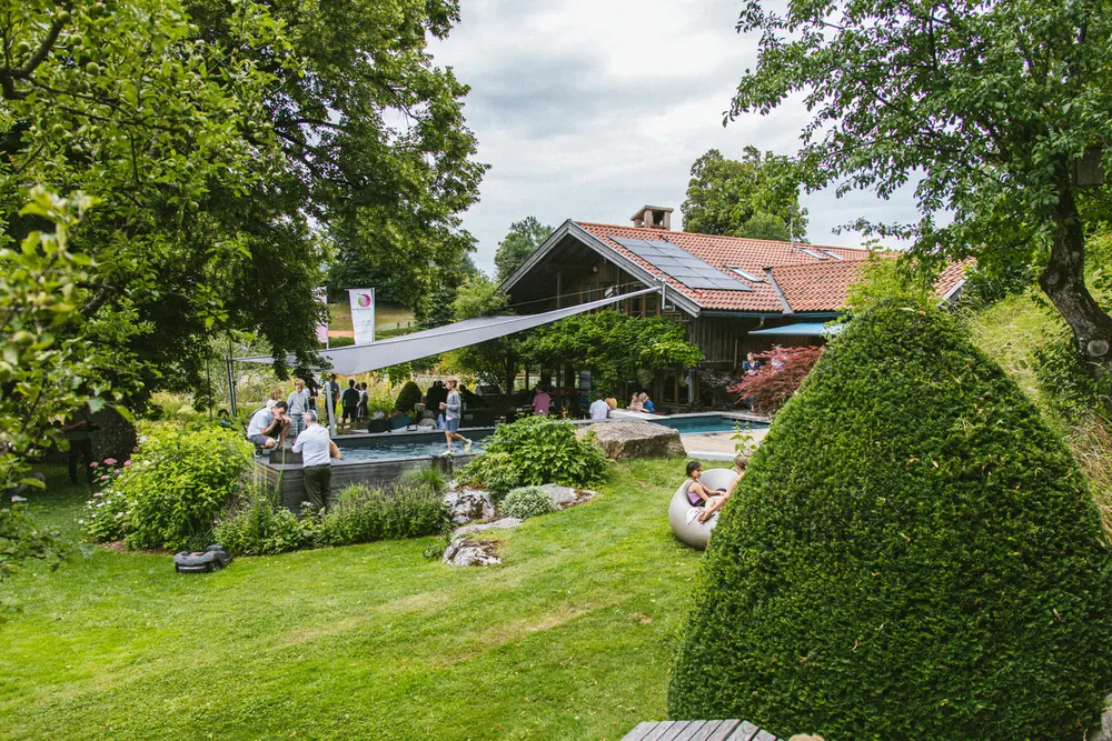 Blick über das Firmengelände mit Rasen, Formschnittgehölzen und dem Living Pool