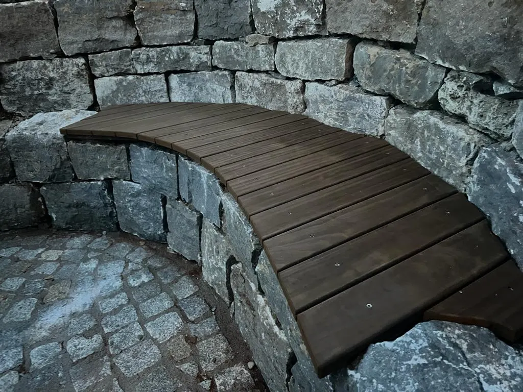 Gebogene Sitzbank aus Holz auf der Natursteinmauer