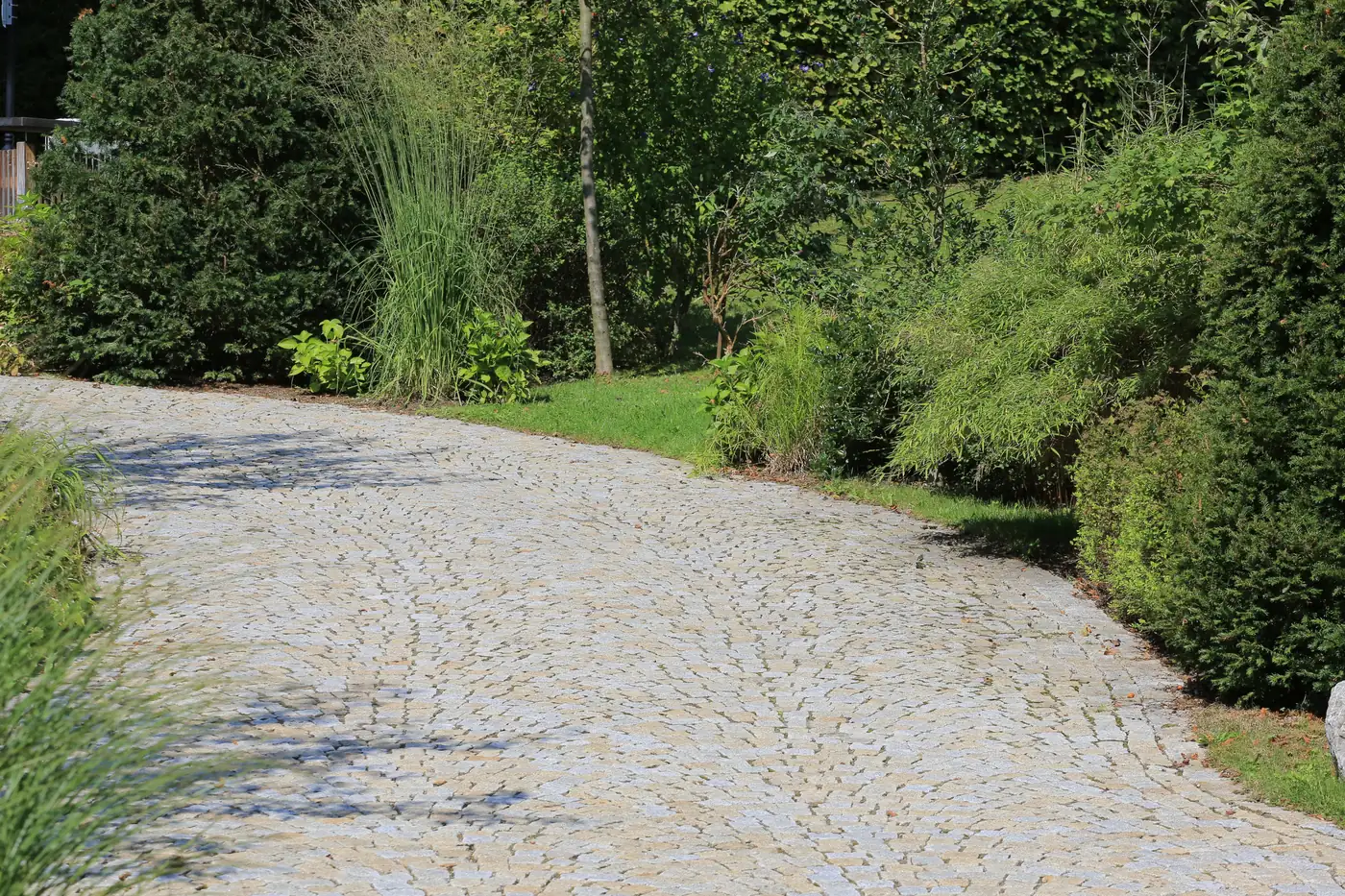 Granit-Kleinpflaster in Bögen, nach vier Jahren eingewachsen zwischen Gräsern und Hecken