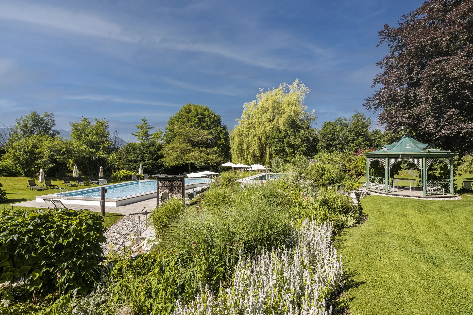 Blick über die Wiese: der Pool, dahinter der grüne Gartenpavillon