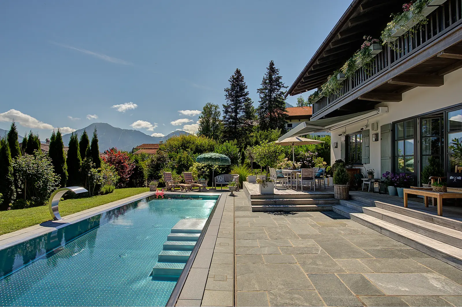 Die Quarzit-Terrasse am Pool, dahinter das Haus mit Holzbalkonen