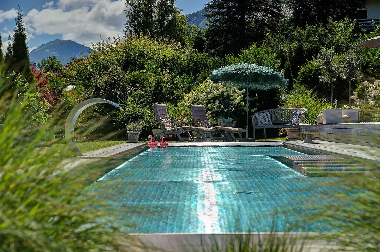 Poolblick: das Edelstahlbecken zwischen Gräsern, hinten der Fontänenbogen
