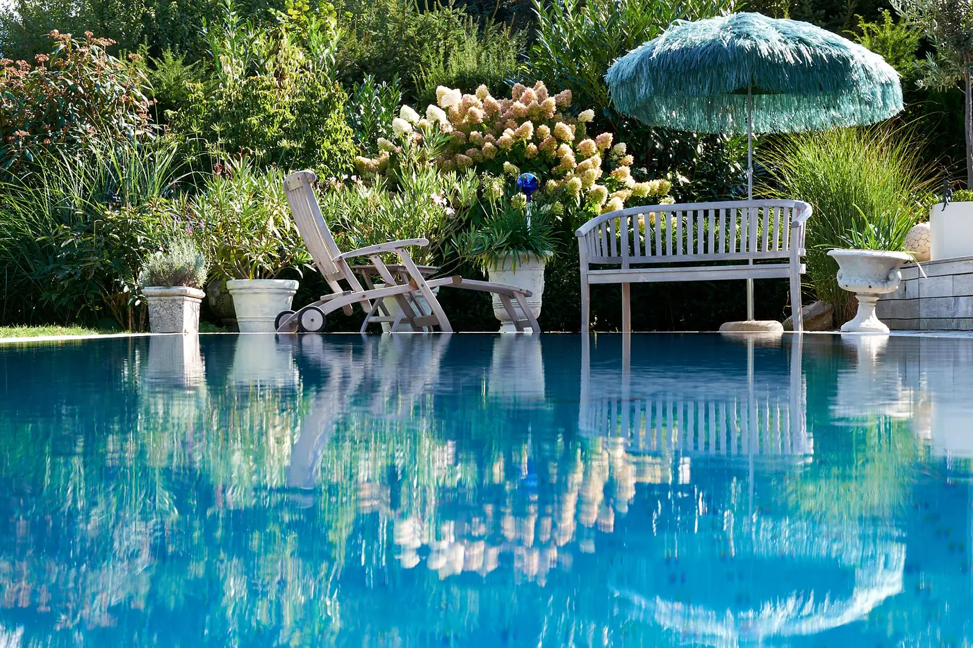 Weiße Bank und Sonnenschirm spiegeln sich im Pool