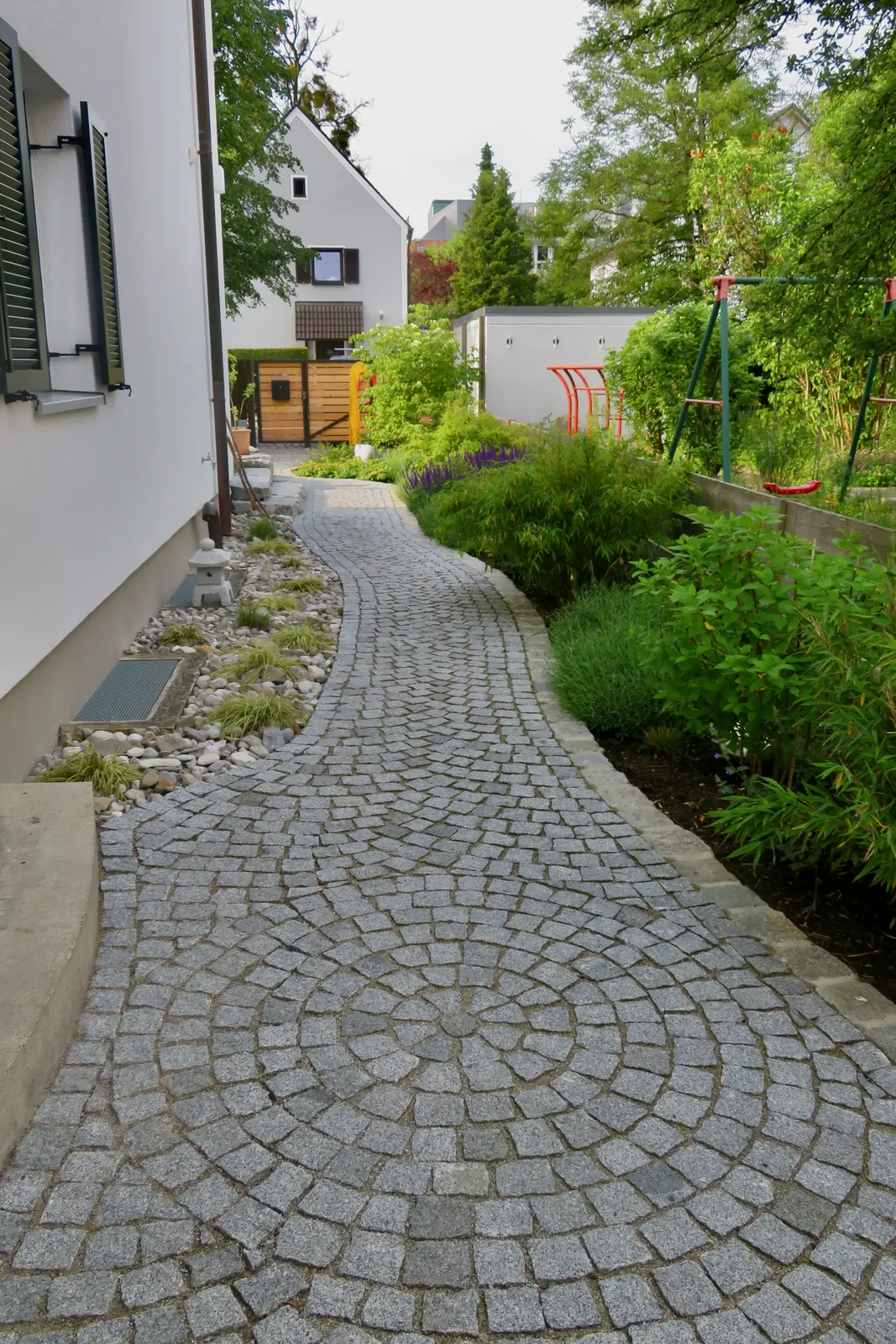 Der Weg aus Kleinpflaster schwingt sich zwischen den Beeten hindurch