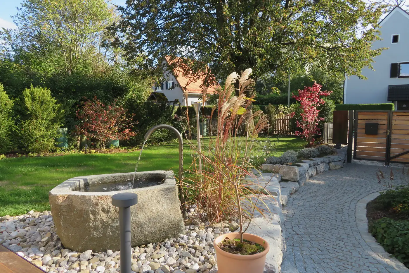 Der Brunnen im Kiesbeet, dahinter Rasen und Gräser