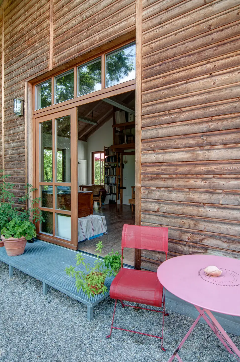 Das Atelier von außen: Holzfassade, große Fenster und ein Sitzplatz davor
