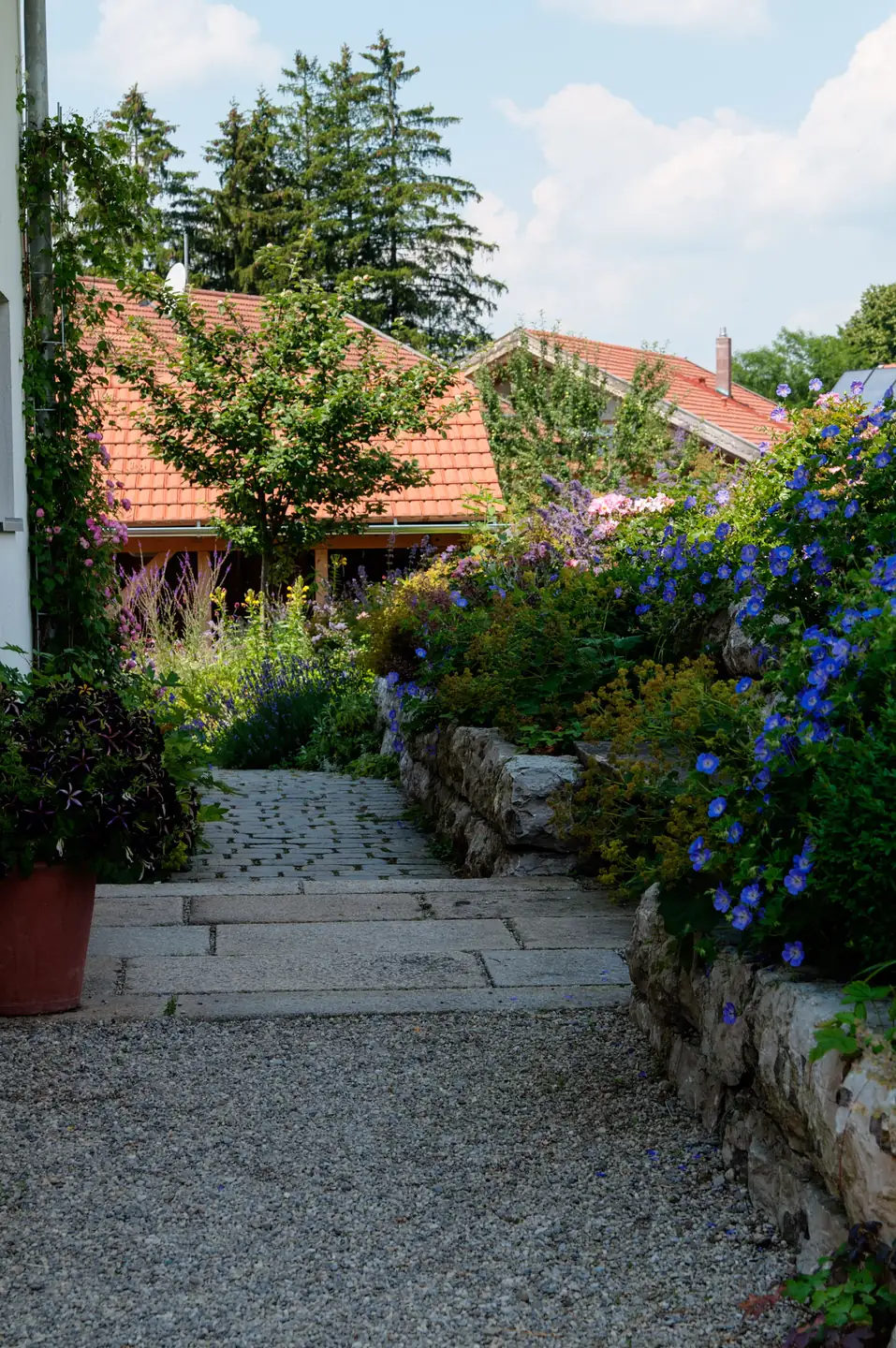 Der Weg zwischen Haus und Staudenbeet, im Hintergrund die Hofgebäude