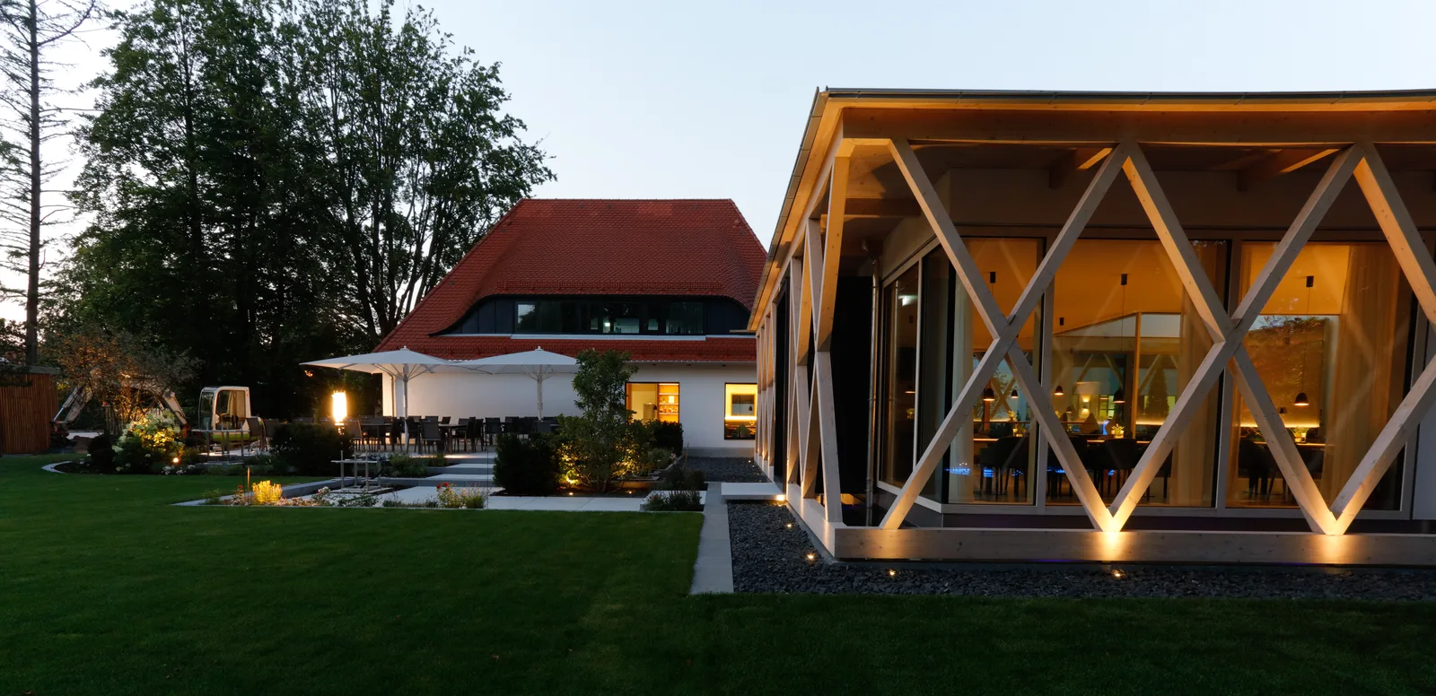 Der Pavillon von der Rasenfläche aus, drinnen warmes Licht, draußen Dämmerung