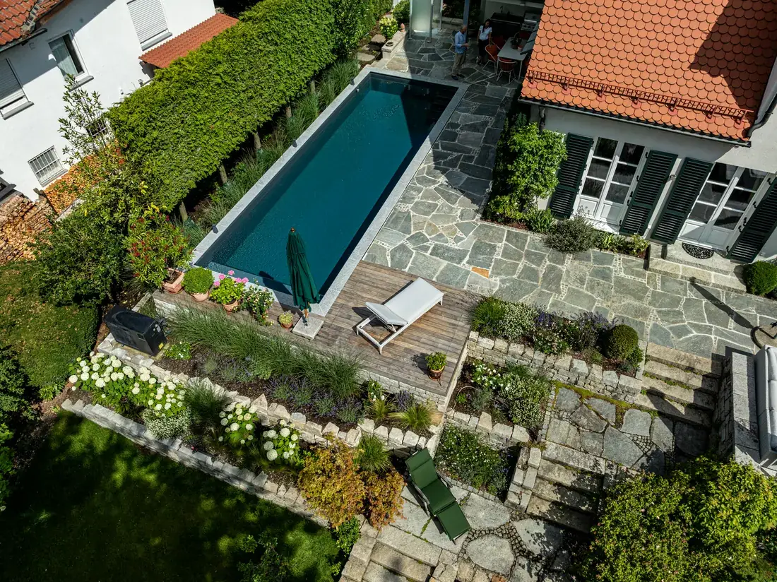 Luftbild des Hanggartens in Tutzing mit Living Pool, terrassierten Natursteinmauern und Terrasse am Haus