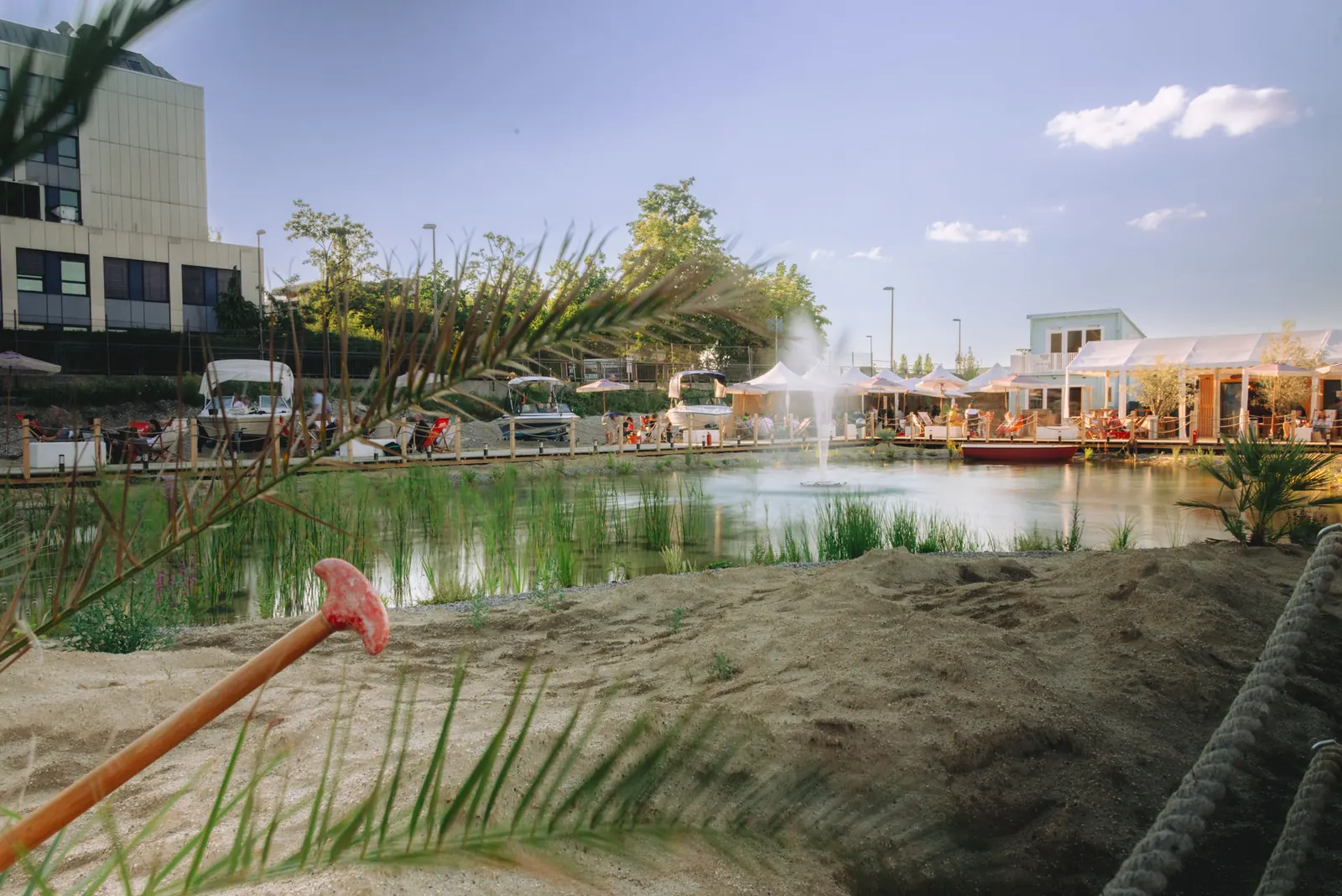 Sandstrand mit Liegen und Palmen am Wasser, im Hintergrund die Bebauung