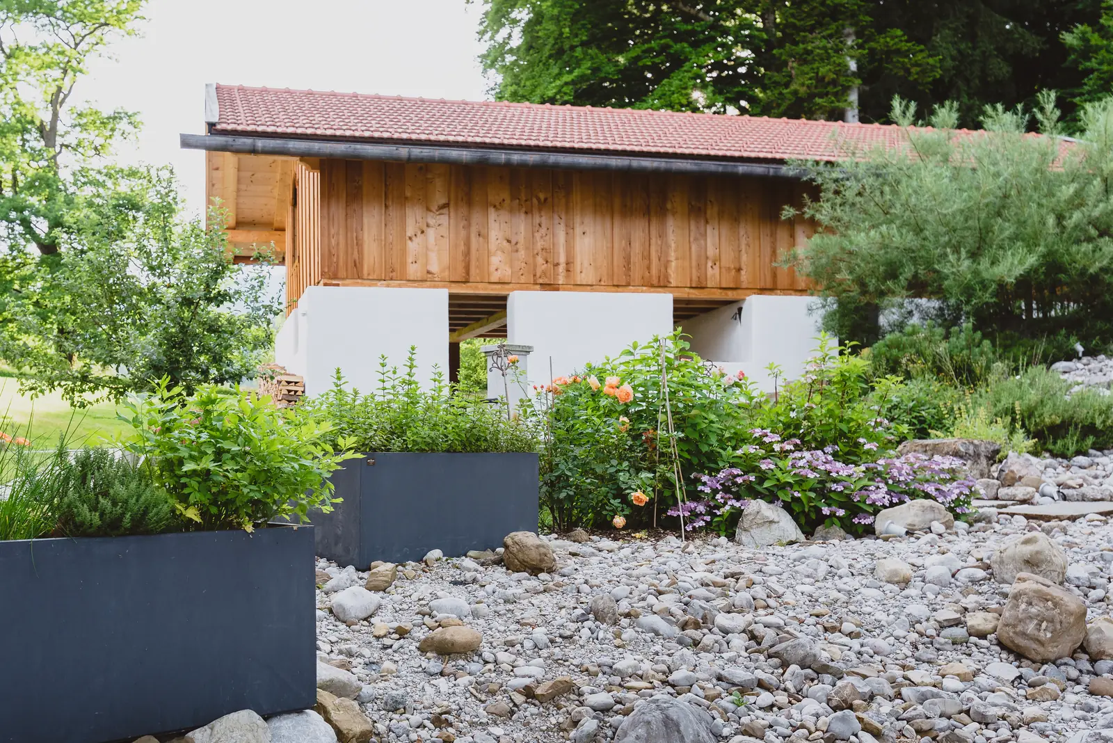 Kiesbeet mit Findlingen und Pflanztrögen vor dem Stadel