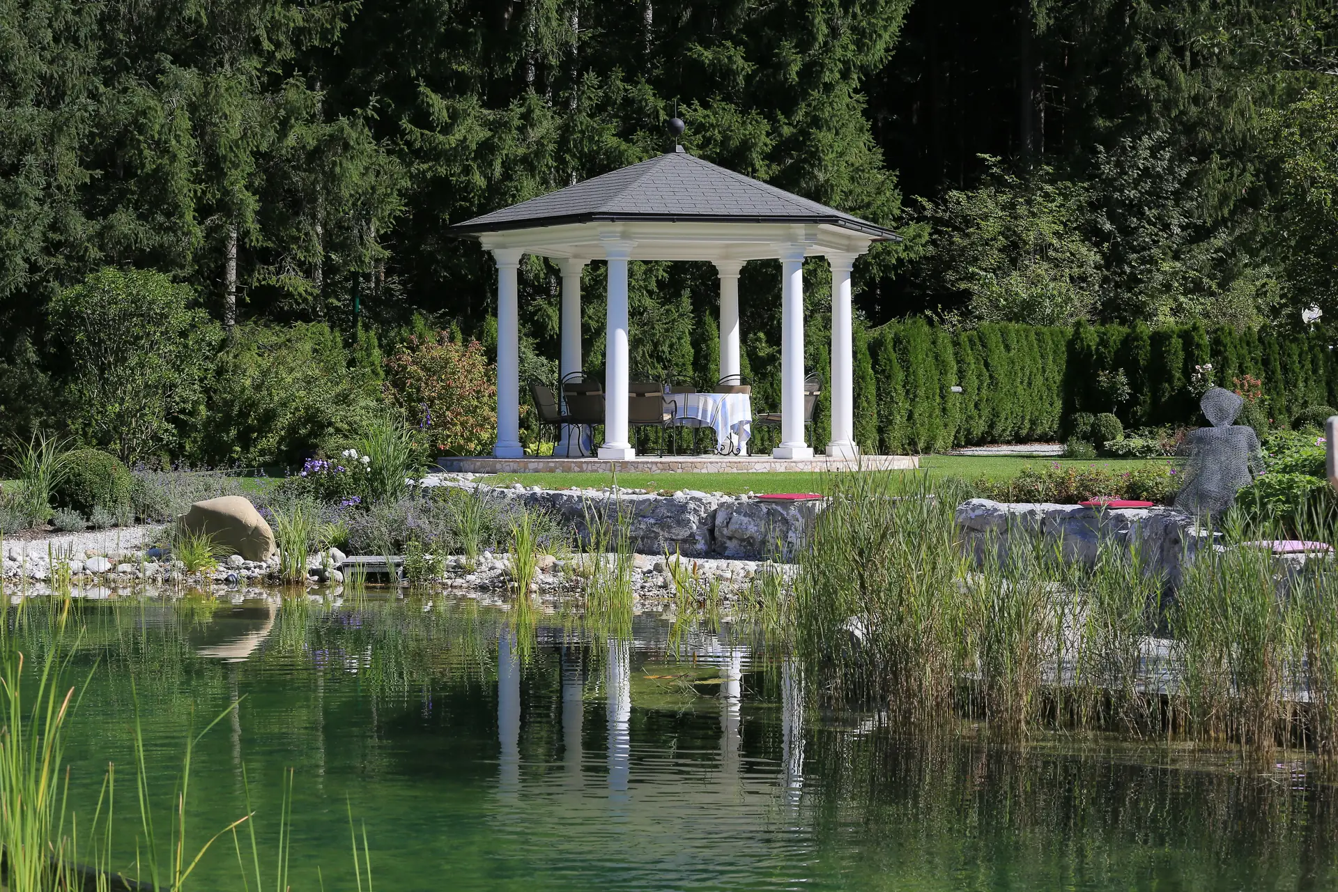 Der weiße Säulenpavillon spiegelt sich im Wasser des Swimming Ponds
