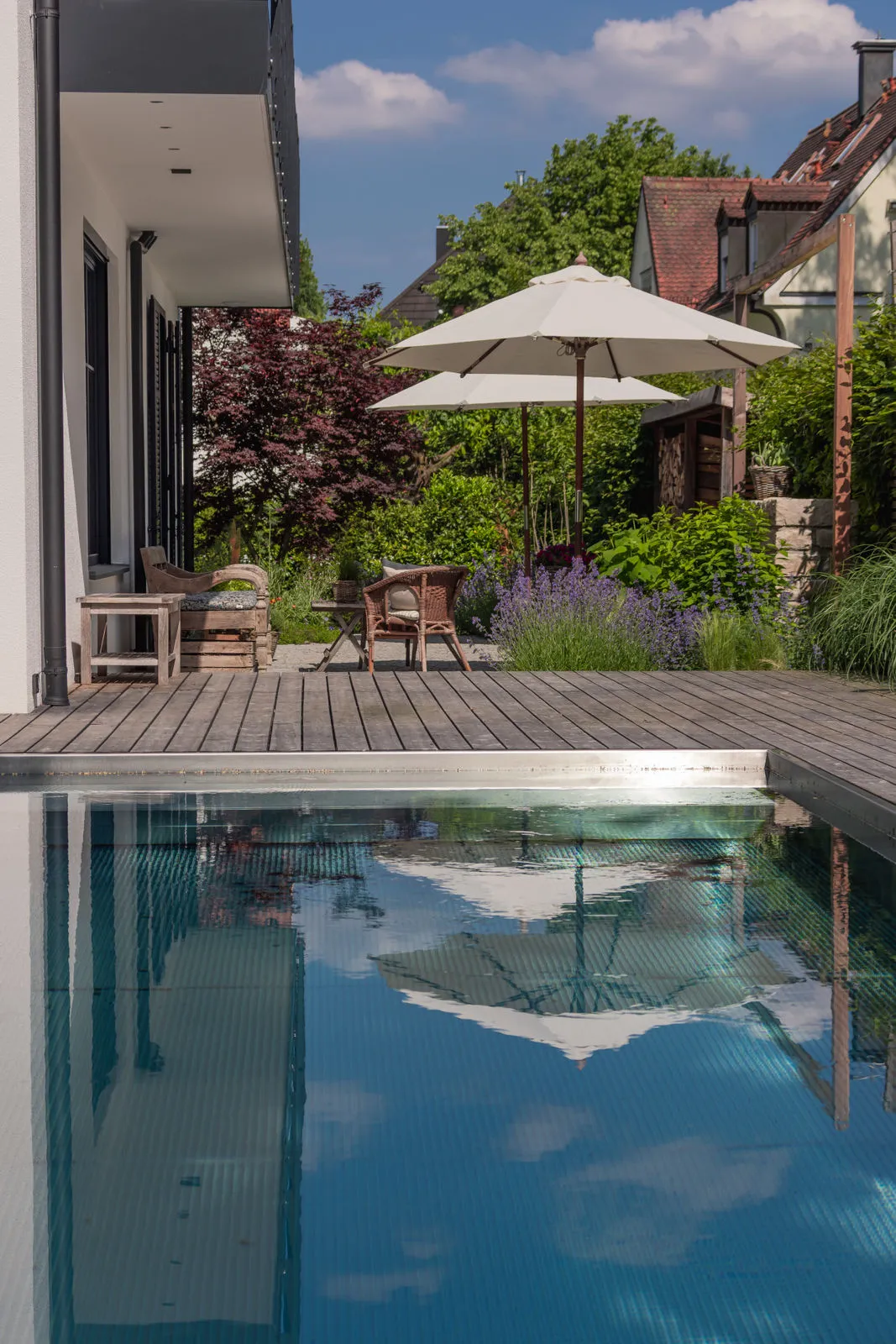 Blick über den Pool: Holzdeck, Schirme und der rote Fächerahorn