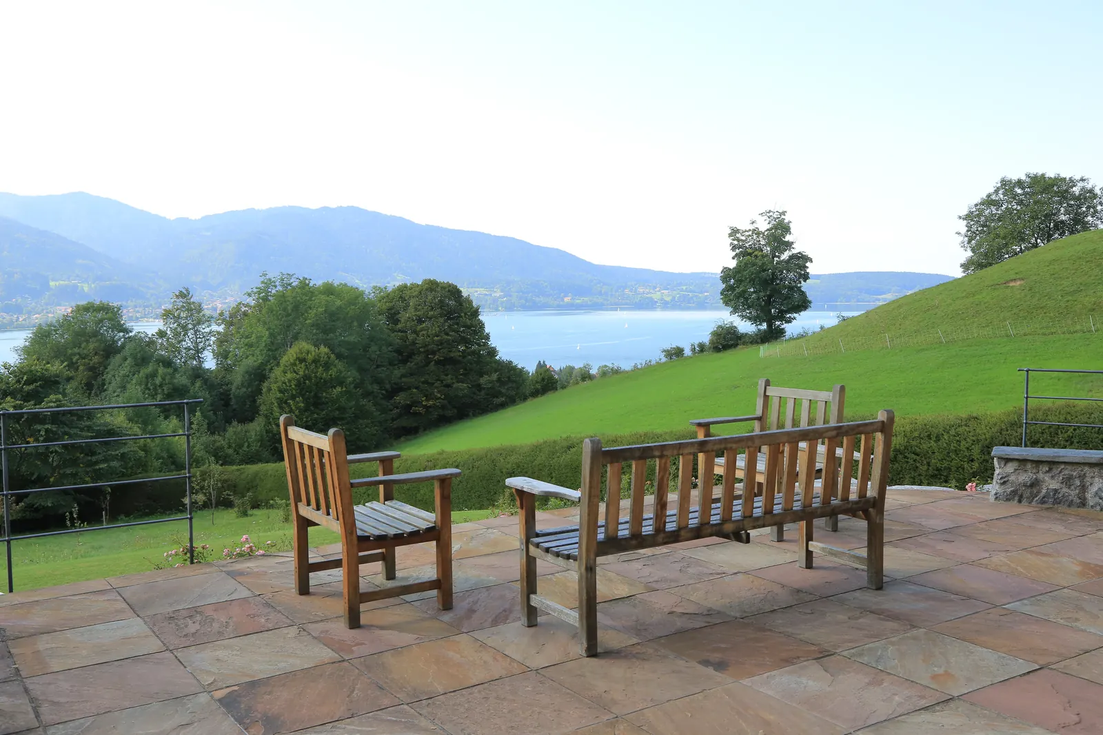Bänke auf der Terrasse, dahinter fällt die Wiese zum See ab