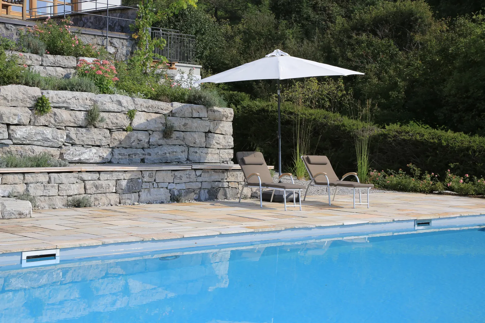 Der Pool liegt vor gestaffelten Kalksteinmauern, der Schirm gibt Schatten