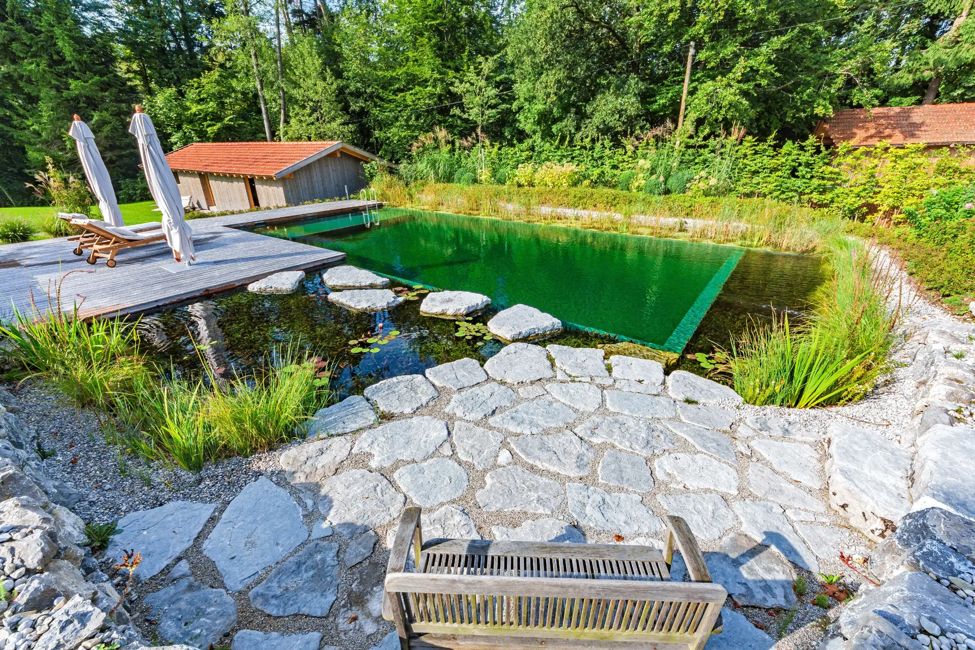 Natursteinplatten am Ufer mit Einstieg und Steg über den Teich