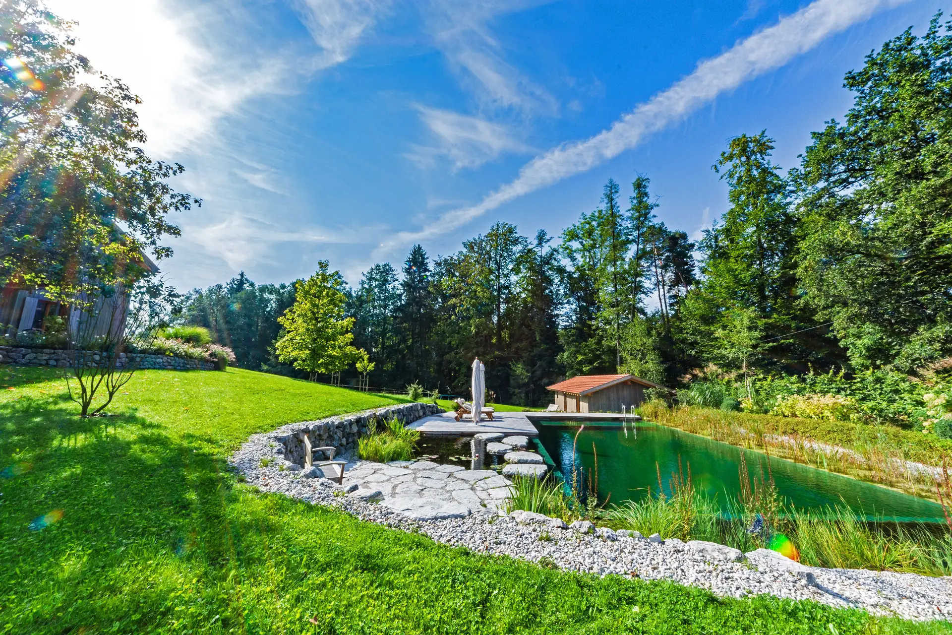 Der Teich von der Wiese aus, gefasst von hellen Natursteinen