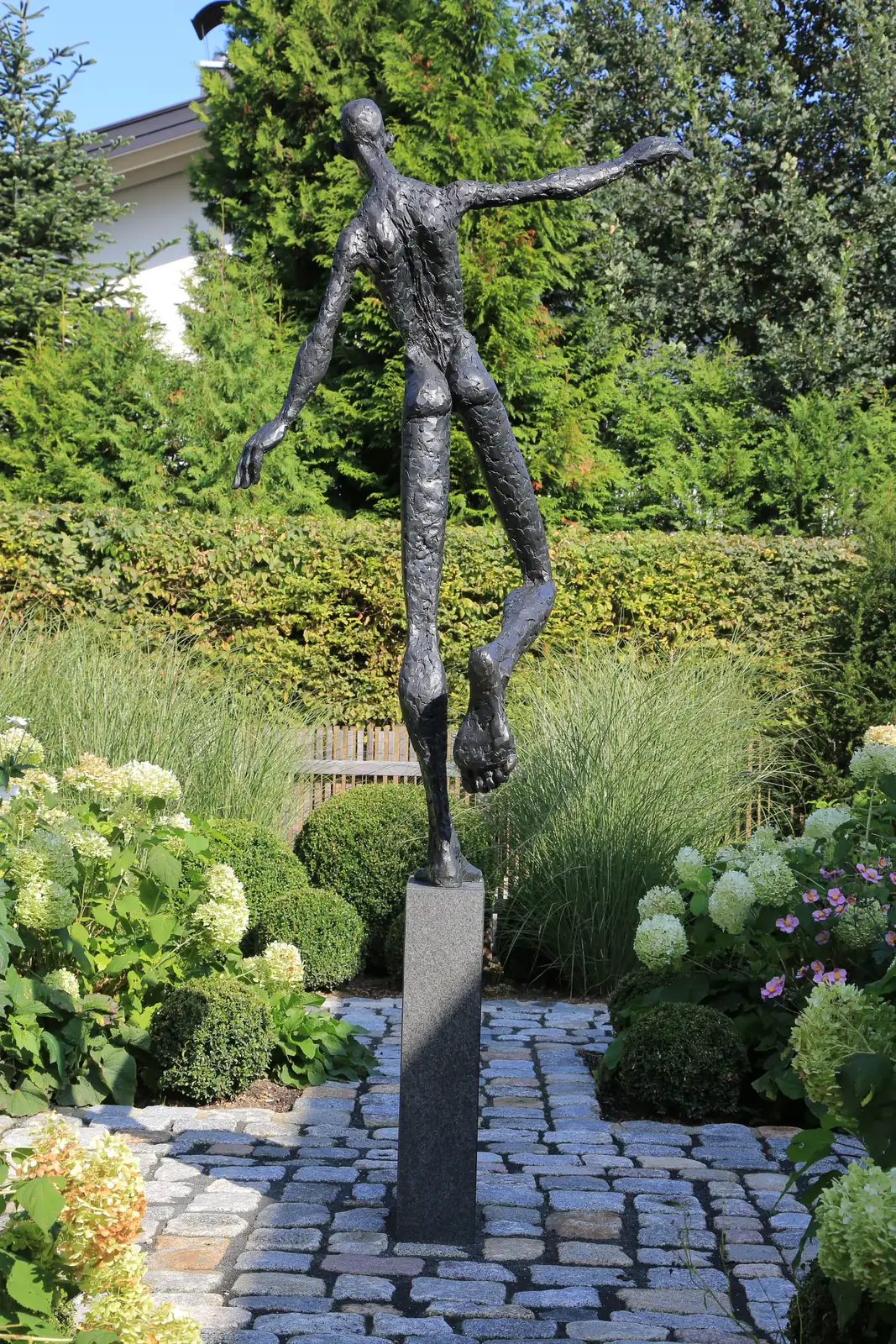 Eine Bronzefigur balanciert über dem Pflasterhof, gerahmt von Gräsern