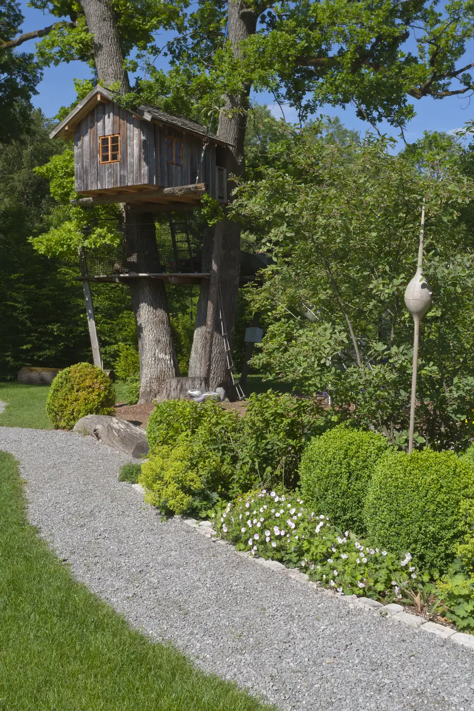 Der Kiesweg mit Formschnitt-Kugeln führt zum Baumhaus in der alten Eiche