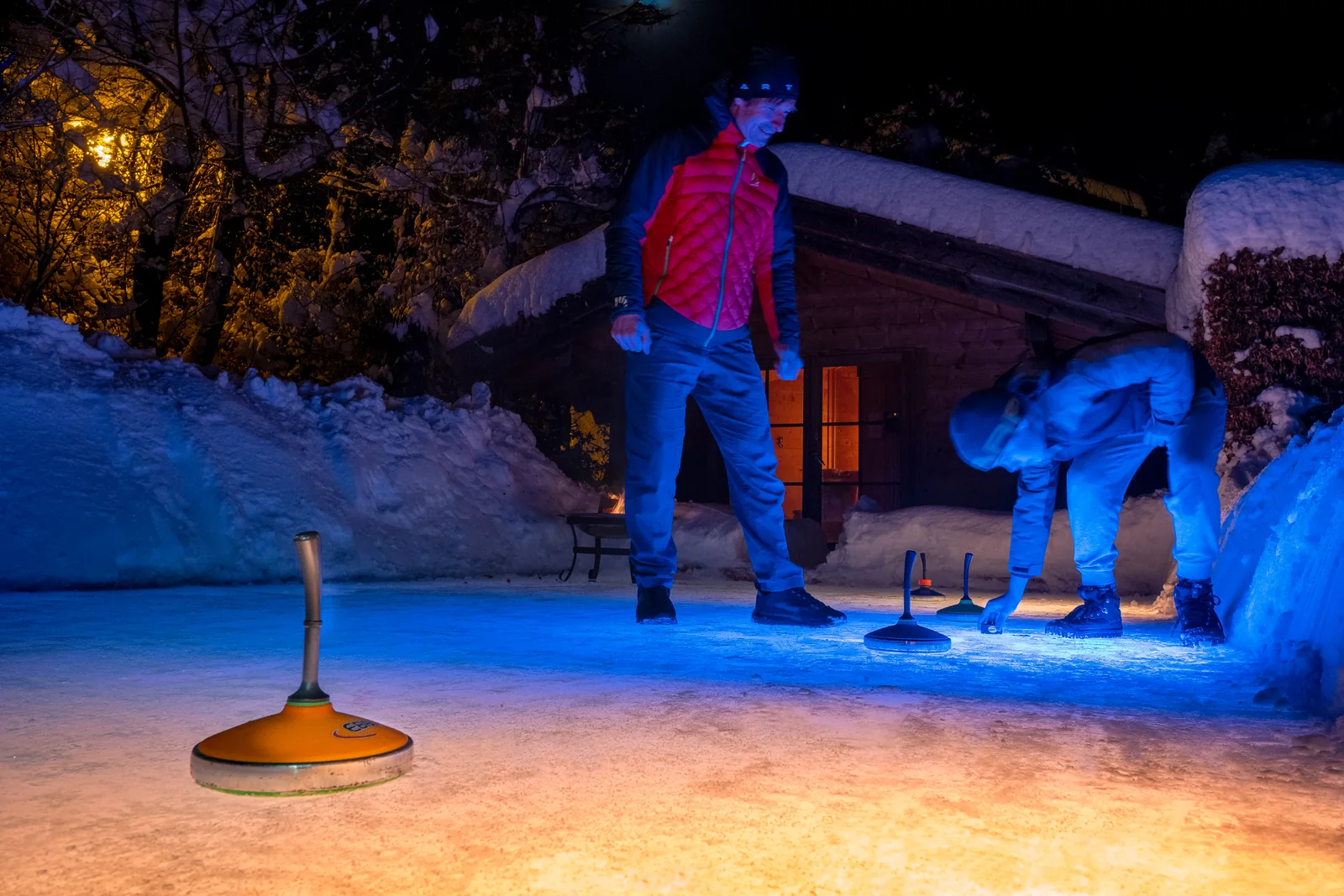 Beleuchtete Eisfläche eines Schwimmteichs bei Nacht mit Eisstock im Vordergrund