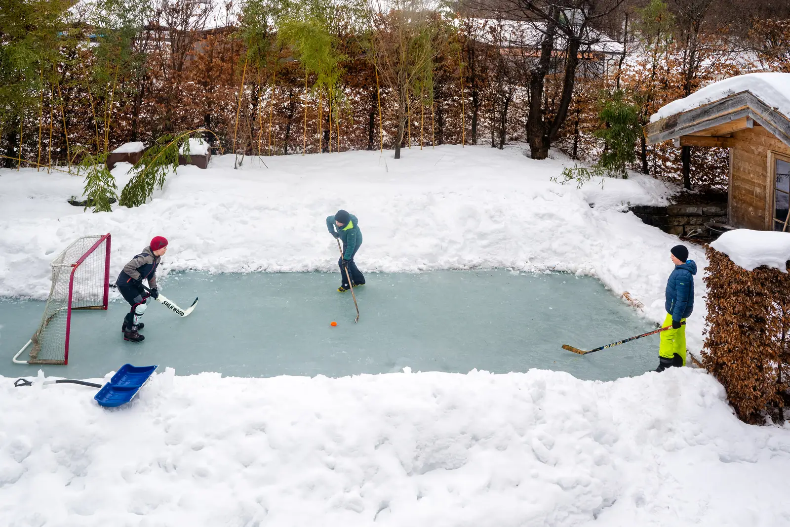 Kinder spielen Eishockey auf einem zugefrorenen Schwimmteich in Lenggries, ringsherum Schnee