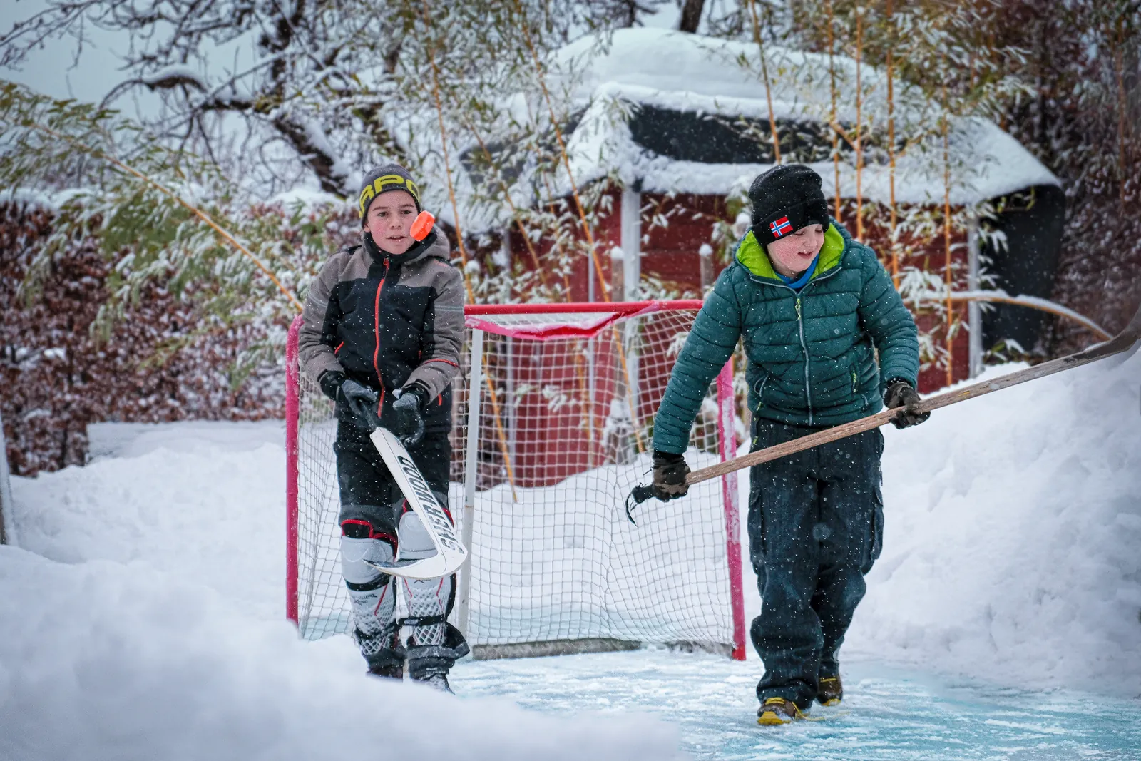 Zwei Kinder mit Eishockeytor auf der gefrorenen Fläche eines Schwimmteichs im Schnee