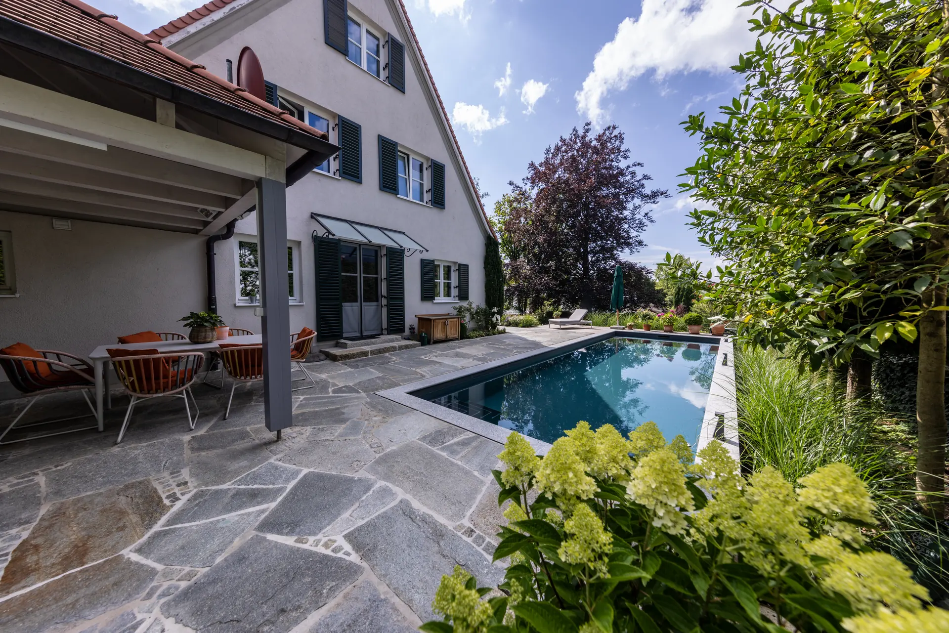 Pool mit Natursteinterrasse und Sitzplatz am Haus