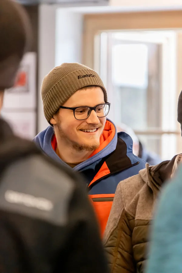 Kollege mit Mütze und Brille grinst in die Runde