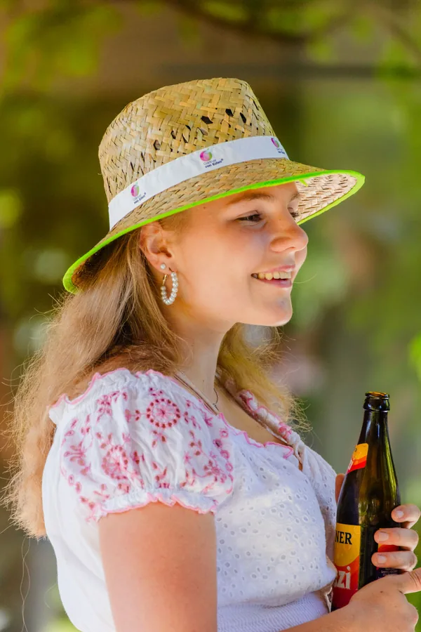 Kollegin mit Strohhut und Limo, lächelnd im Grünen