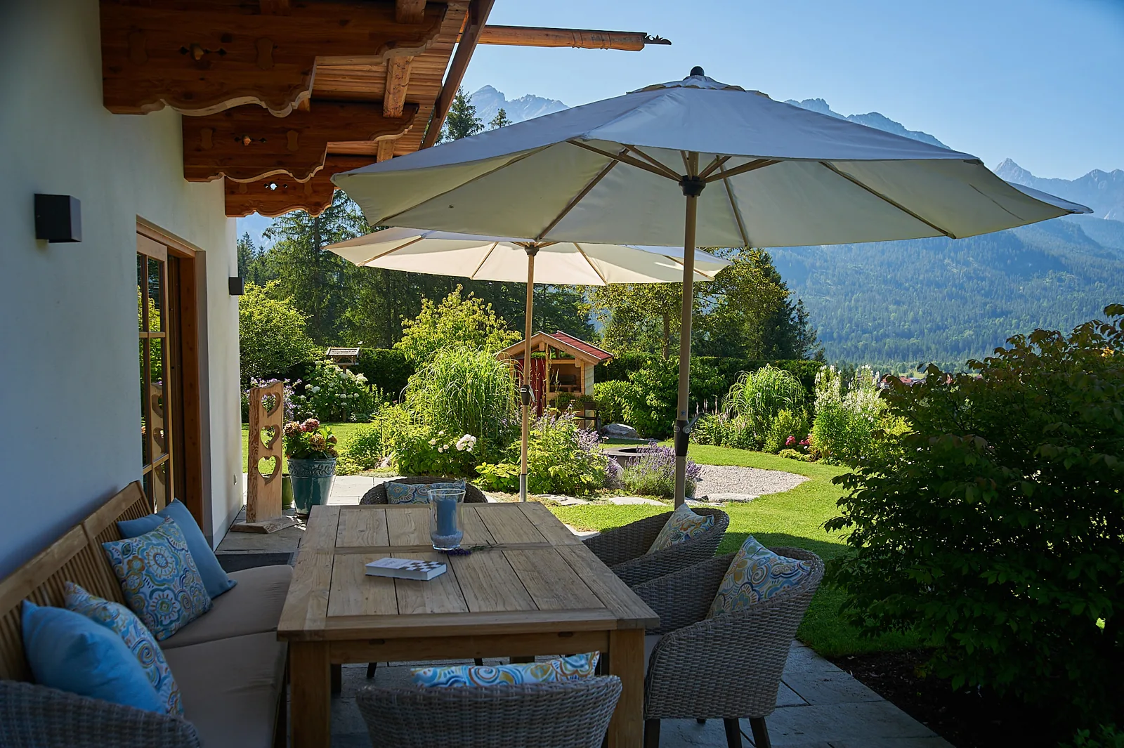 Terrasse mit Sonnenschirm und Garten, dahinter die Berge des Oberlands